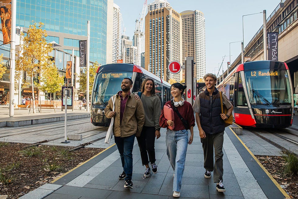 Um grupo de estudantes internacionais caminha em uma plataforma de trem em Circular Quay, Sydney. Imagem de cortesia da Destination NSW