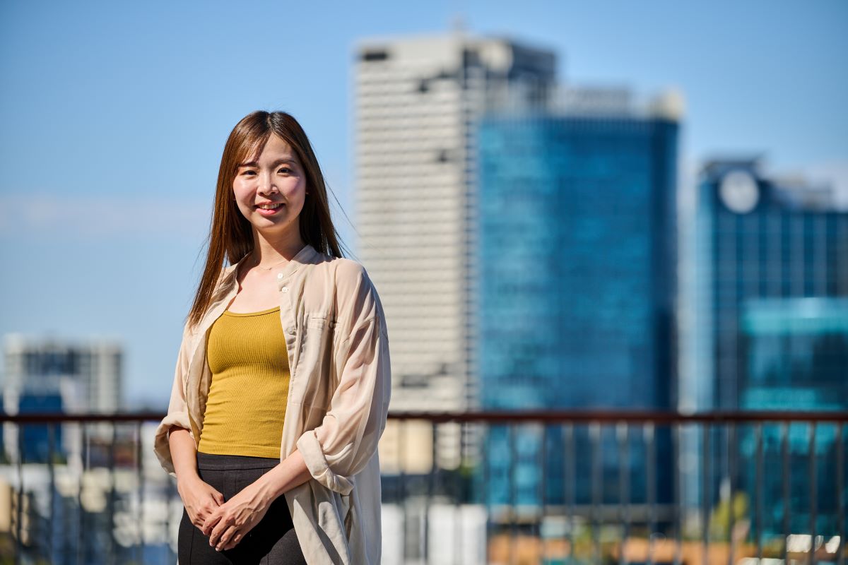 International student, Tsubasa smiling with some city buildings in the background