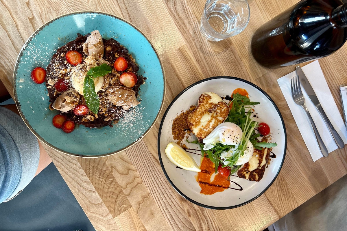 Two breakfast dishes on a cafe table. One is acai and the other is eggs and halloumi .