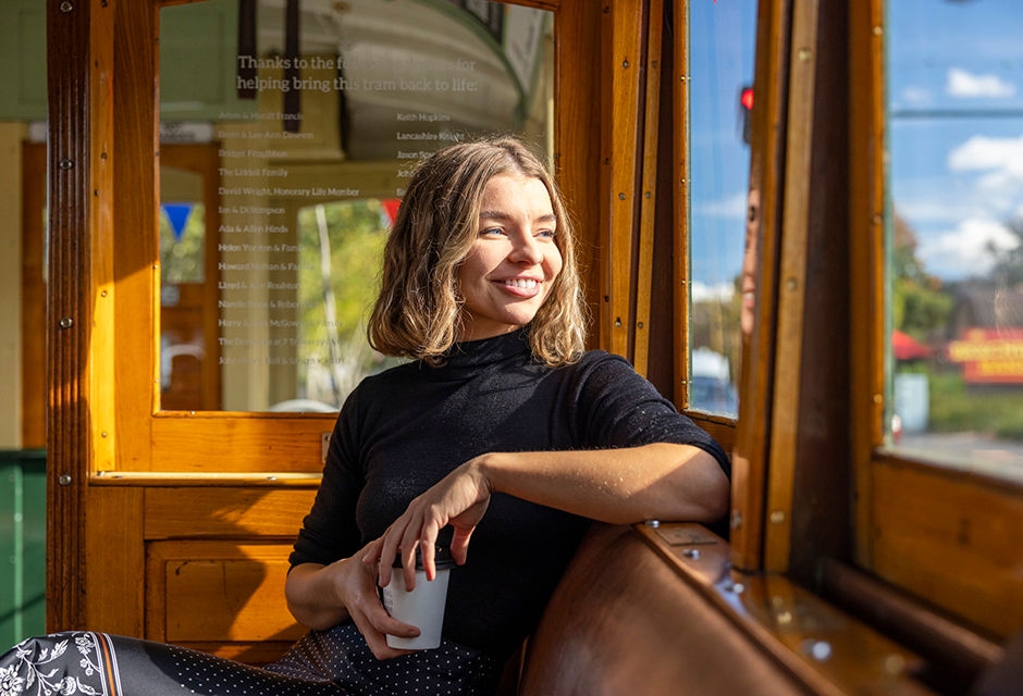A smiling girl sits with a coffee looking out the window of a Bendigo tram. 