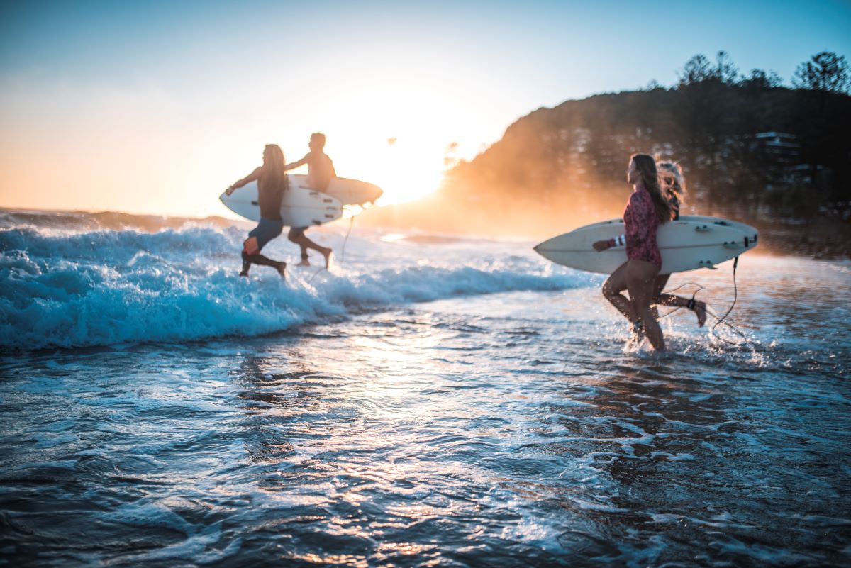 Four people running into the water for a surf