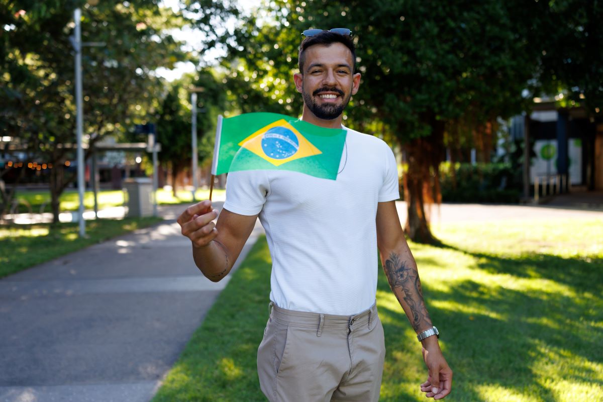 International student, Bernardo, holding the Brazilian flag and smiling