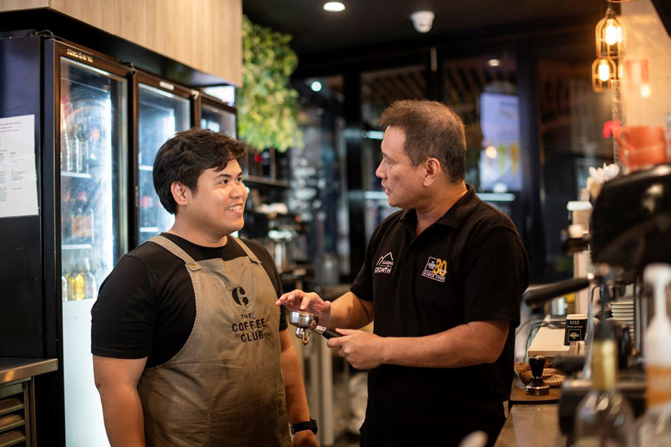 A café owner is teaching an international student how to make coffee. 