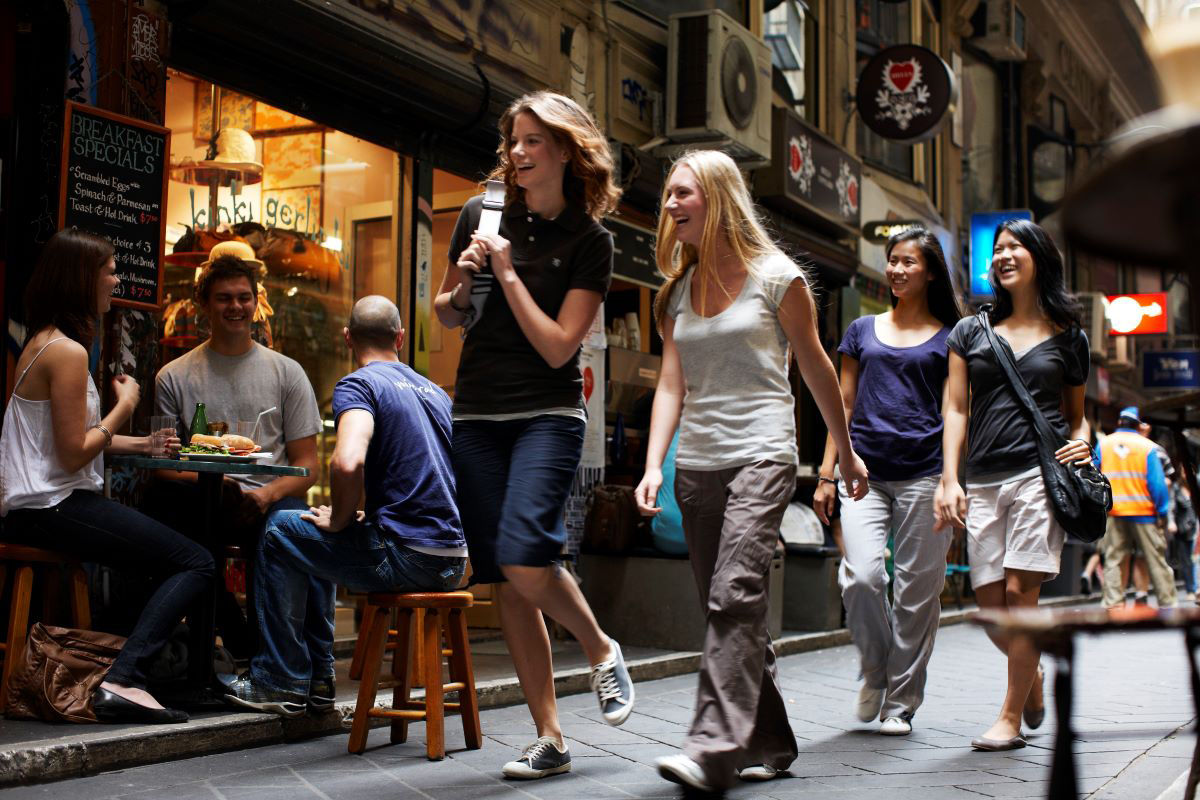 A group of female international students are lauging and walking down a busy Melbourne street