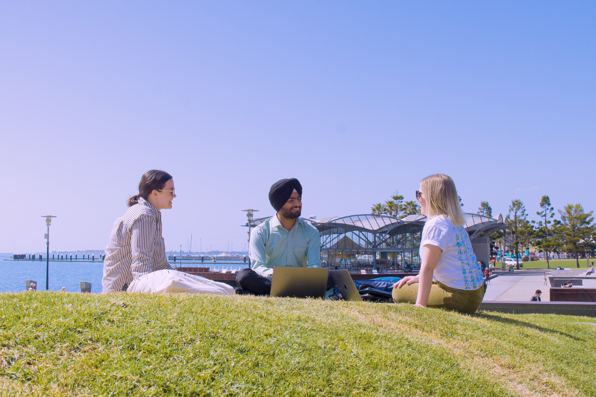 Three international students sitting by the water chatting