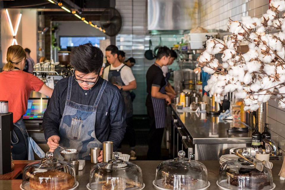 A male international student is making coffees in a busy cafe. 