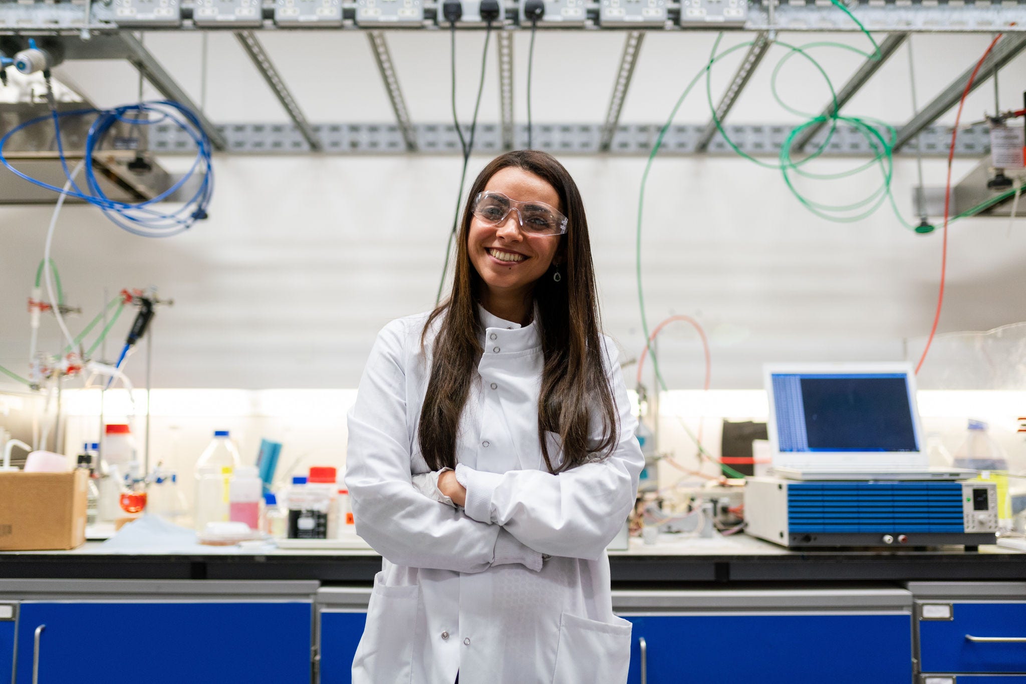 Smiling female engineering student wearing lab coat and safety glasses.