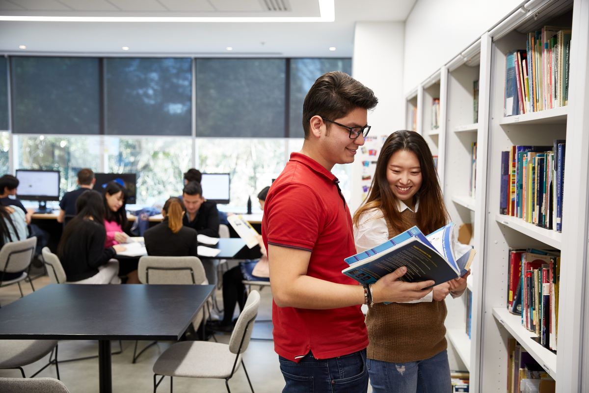 Two international students are looking through a book at a university library 