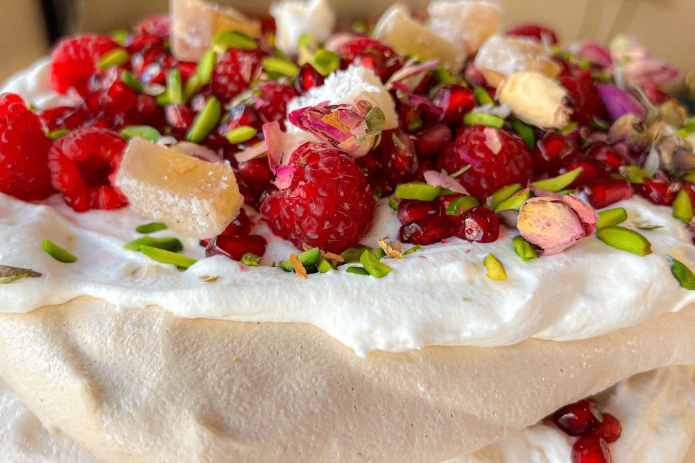 A close-up of an Australian classic dessert, pavlova. It is covered in cream and strawberries.
