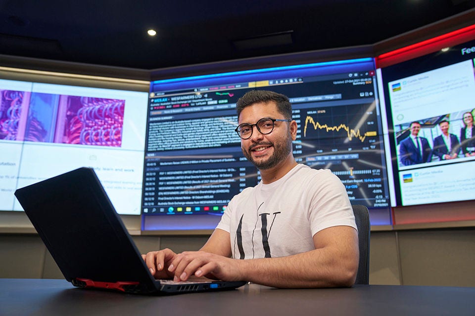 A student working on his laptop sitting in front of large screens. 