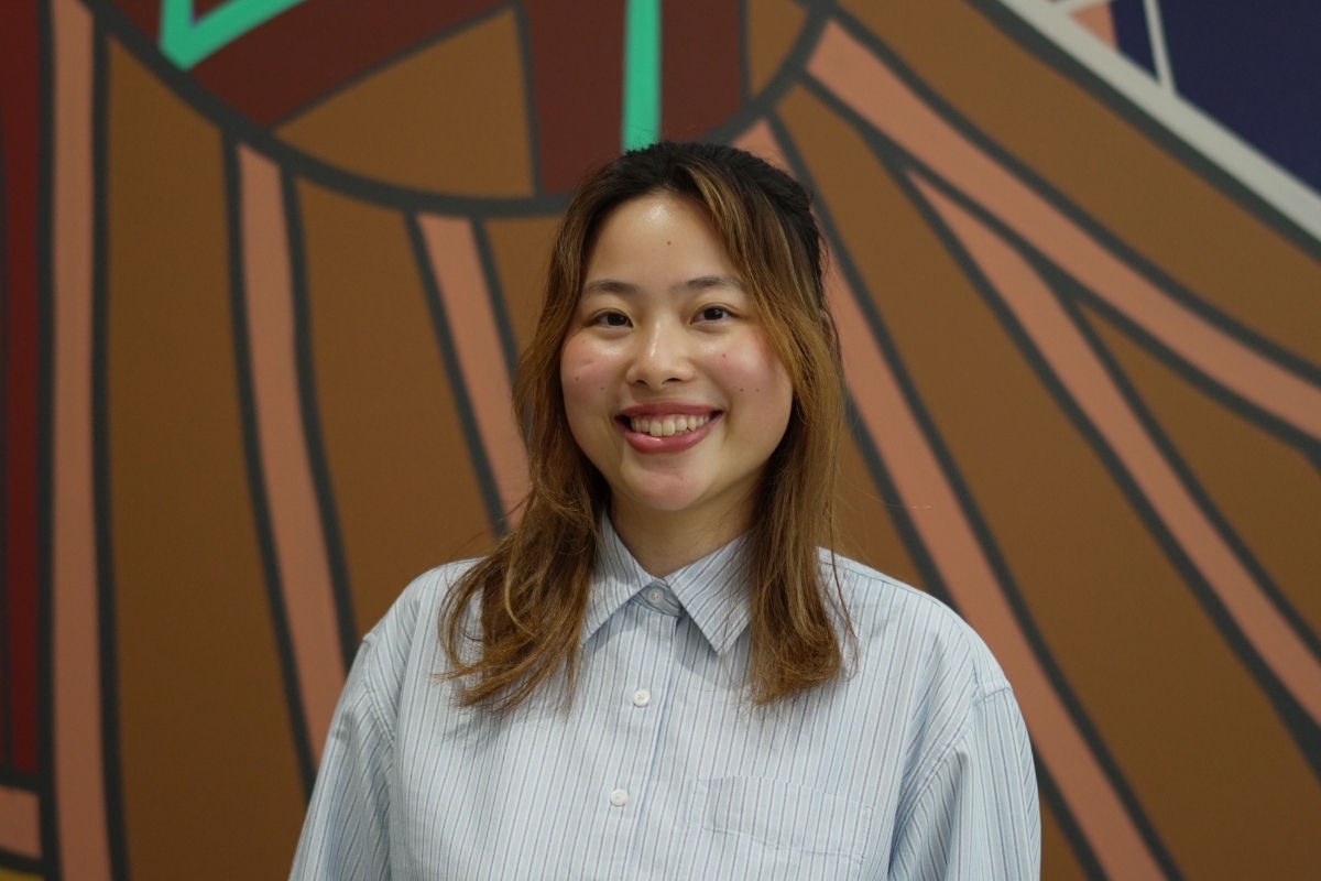 A photo of international student, Akiho, smiling in front of a brightly coloured wall
