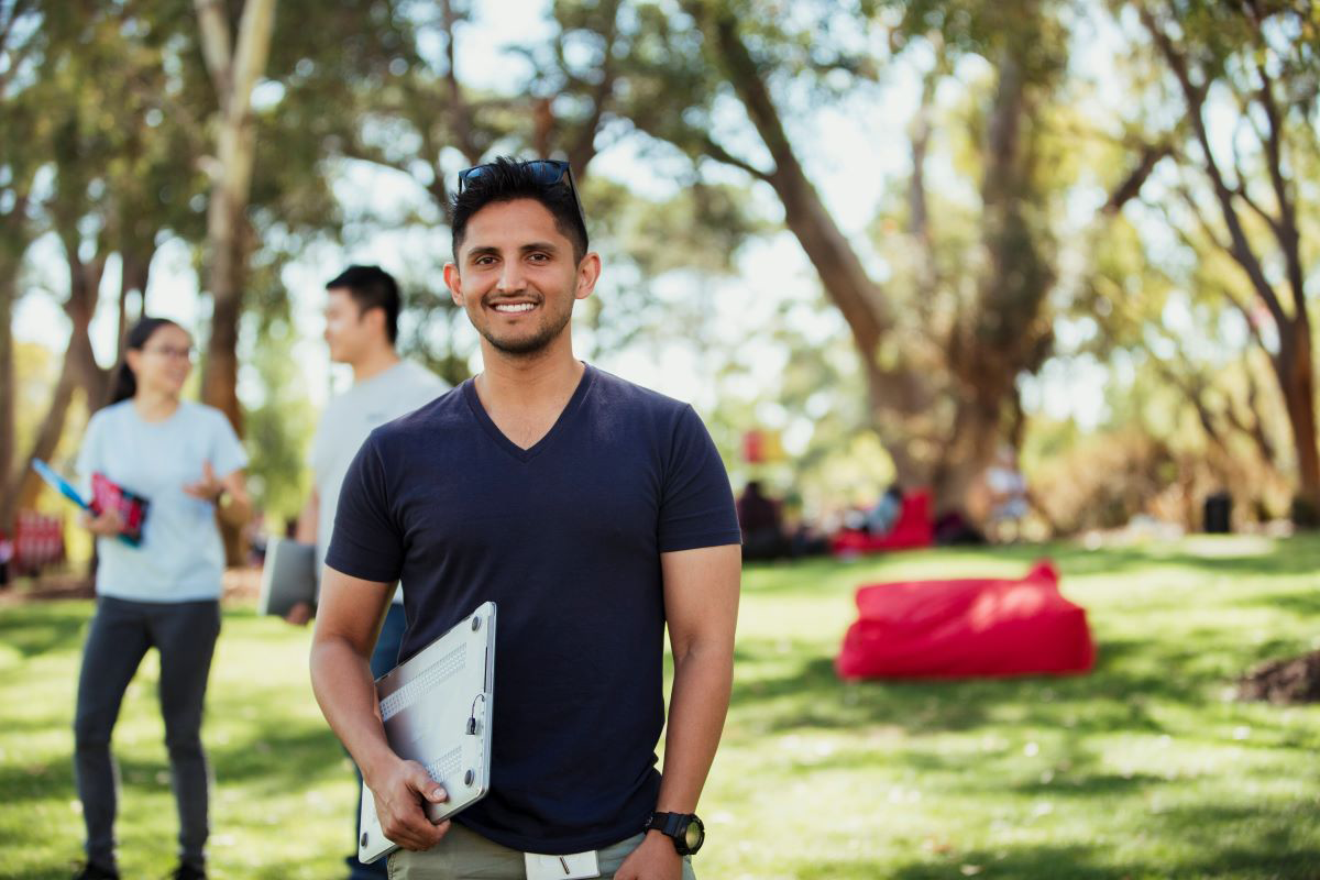 An international student standing in an Australian park holding a laptop. 