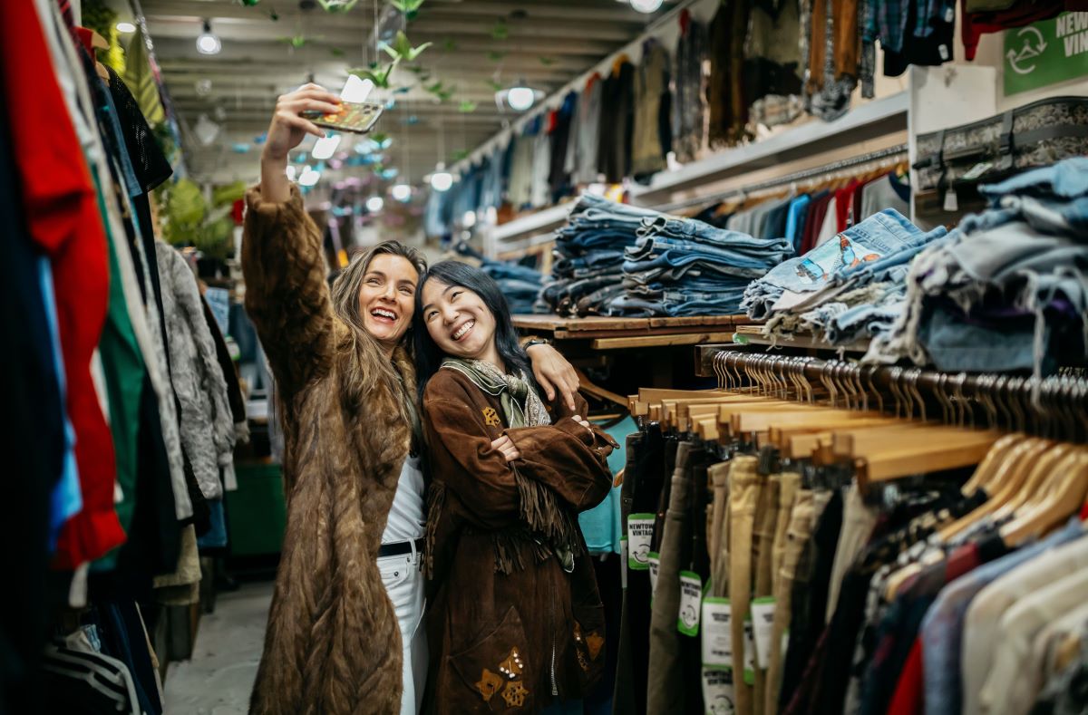 Two friends trying on coats at a secondhand shop