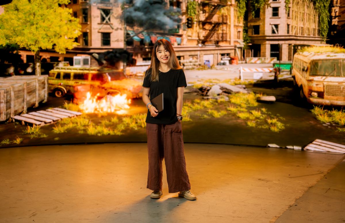 Lurong standing in front of a panited wall with a street scene behind her