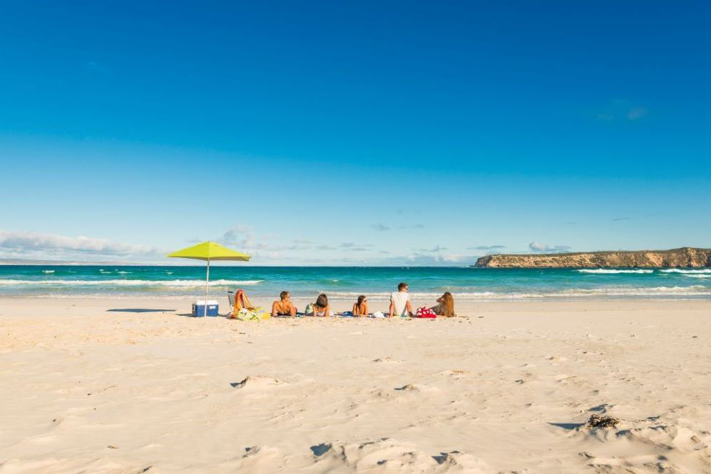 A group of students sit on an Australian beach looking out at the water