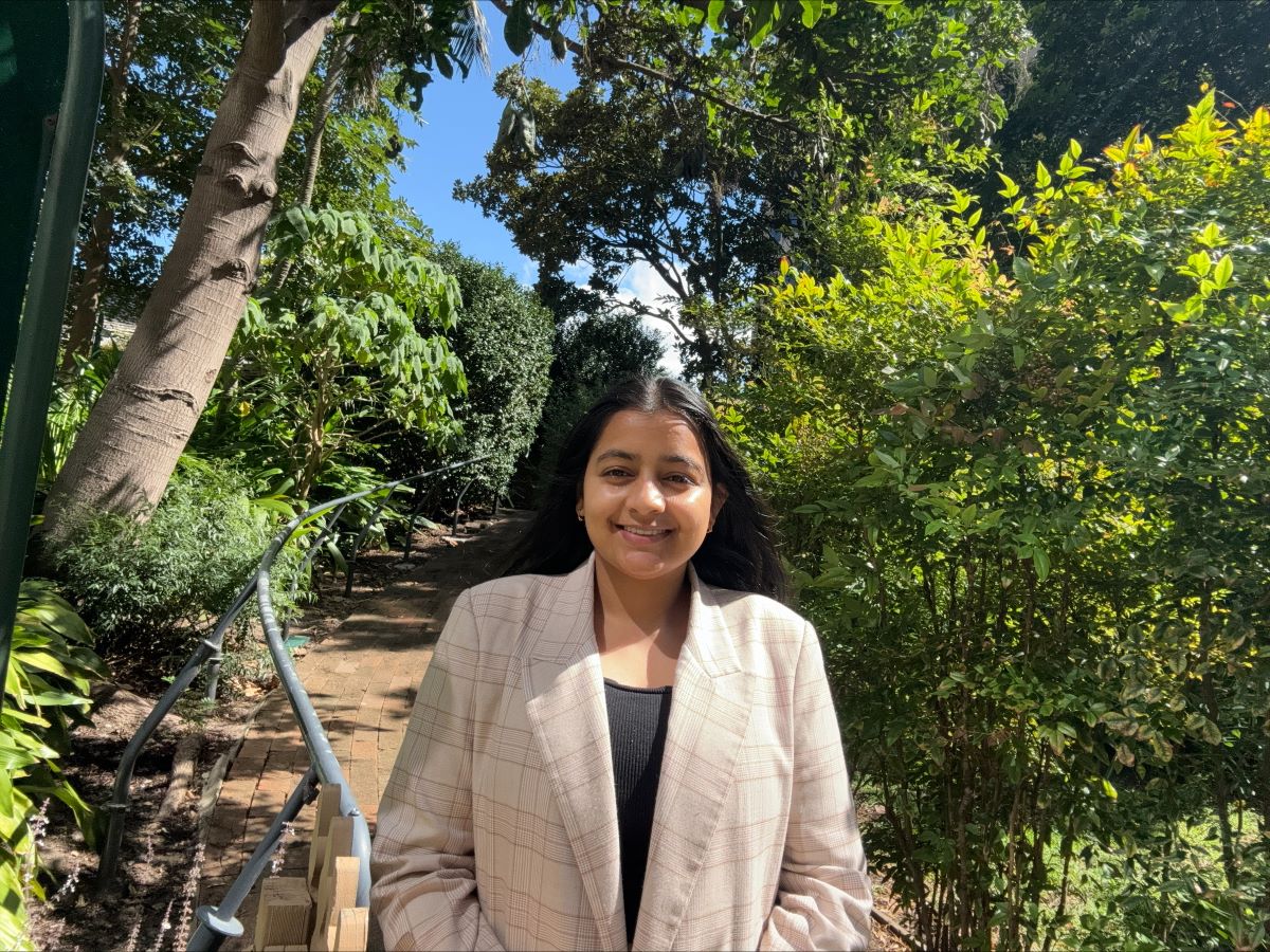 International student, Neha, smiling with trees in the background