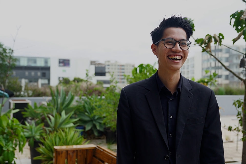Austin, a Law and International Relations Graduate and Legal Clerk at AKN & Associates. is smiling in a garden surrounded by buildings