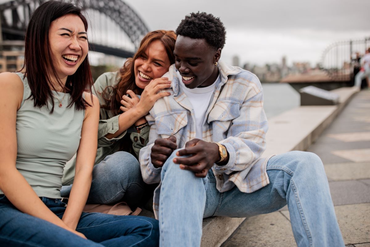 three friends, from different backgrounds, laughing in front of the Sydney Harbour Bridge