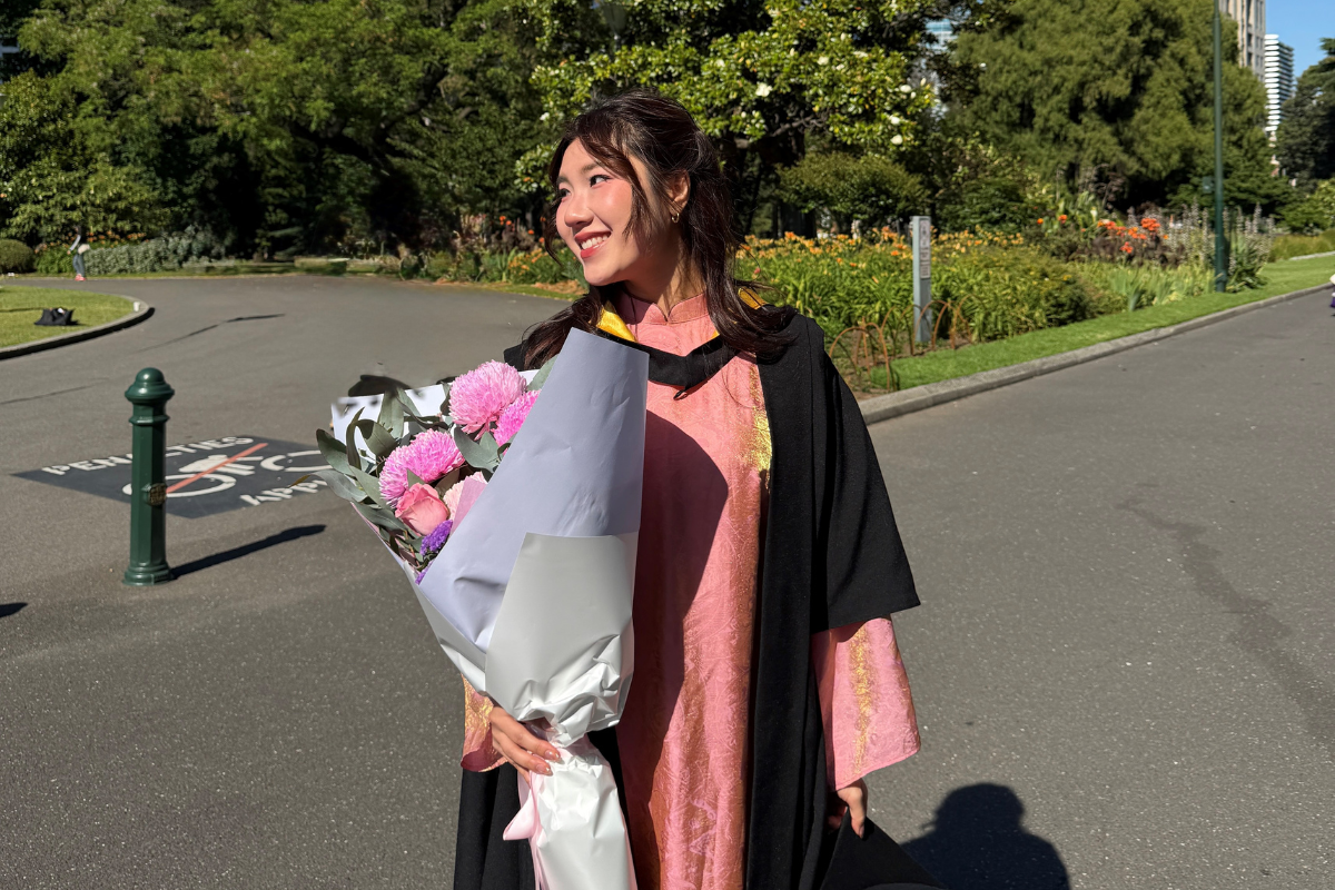 Vicky holds a bunch of flowers and is wearing her graduation gown