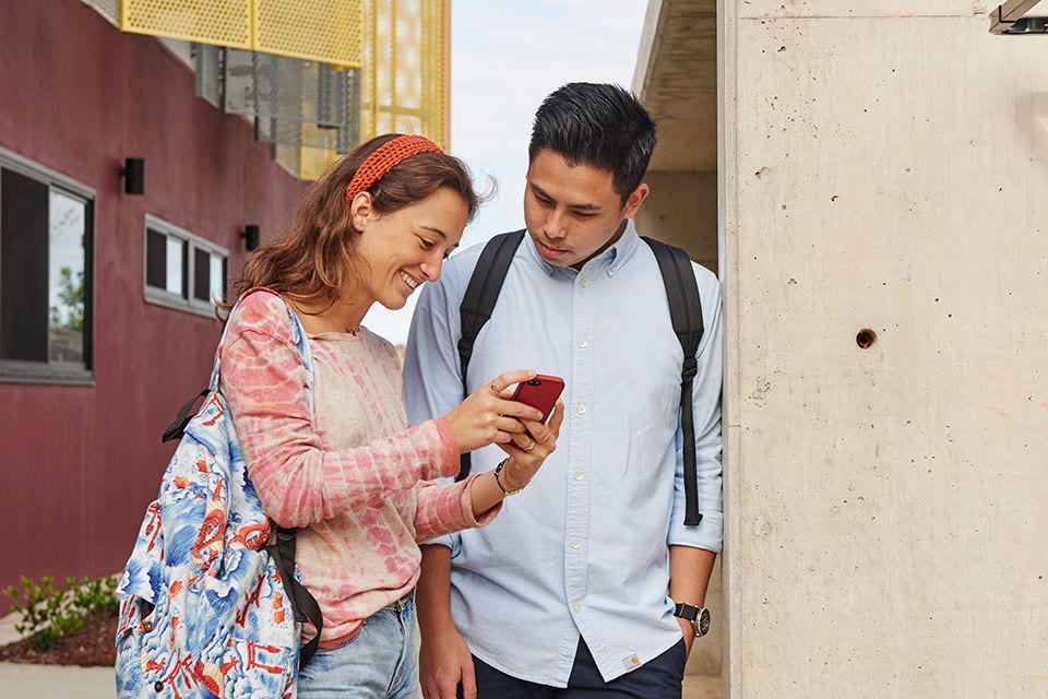 Two students look at a smartphone. 