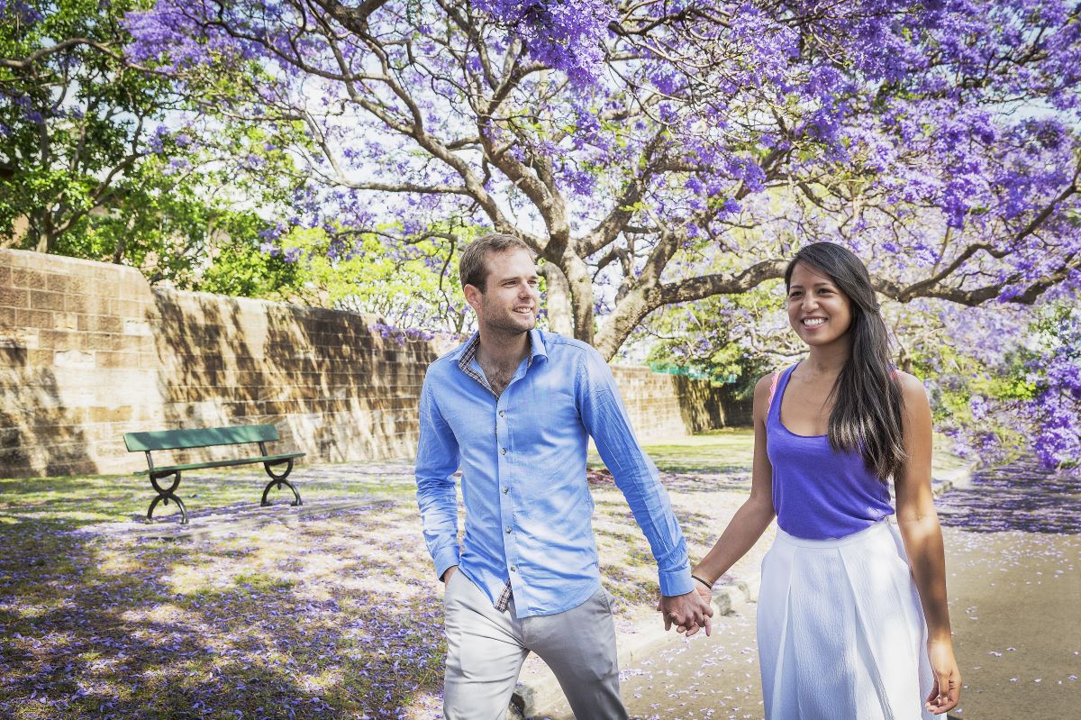 A couple walking under jacaranda trees and holding hands