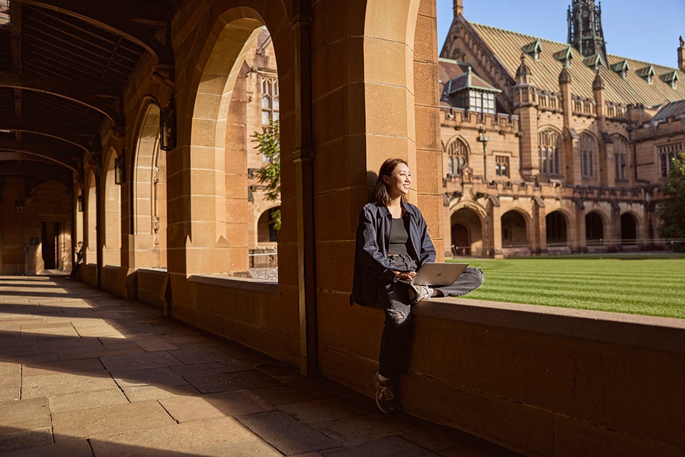 An Asian student working on her laptop in The University of Sydney Great Hall Quadrangle .