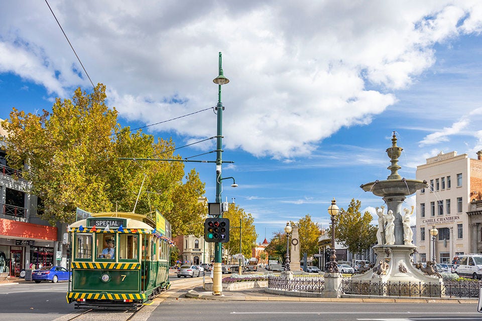 One of Bendigo’s vintage trams travelling down a stretch of road lined with autumn trees and distinct, historic buildings. Image courtesy of Visit Victoria.  