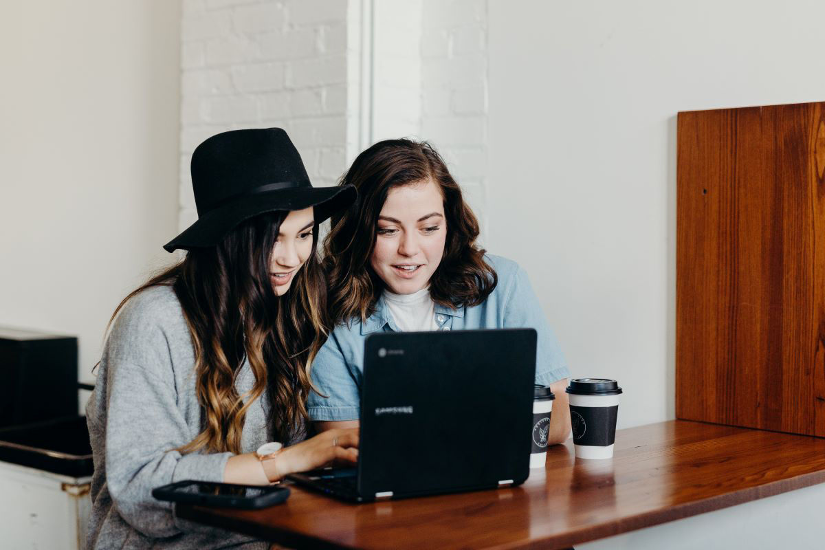 Two female students sit with coffees browsing on a laptop
